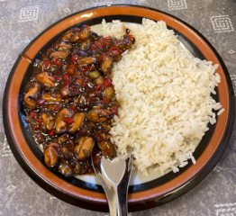 A plate the left side of which is filled with clams with black bean sauce and the right side of which is covered in white rice.