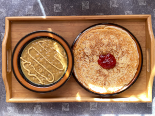 A bowl of swedish pea soup topped with mustard to the left of a plate of swedish pancakes with a dollop of strawberry jam on top.